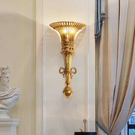 The golden French designer wall lamp installed on a light wall beside a curtain and classical bust sculpture.