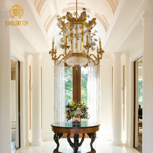 A luxury chandelier installed in a grand foyer with classical columns, illuminating a round console table with a floral centerpiece.