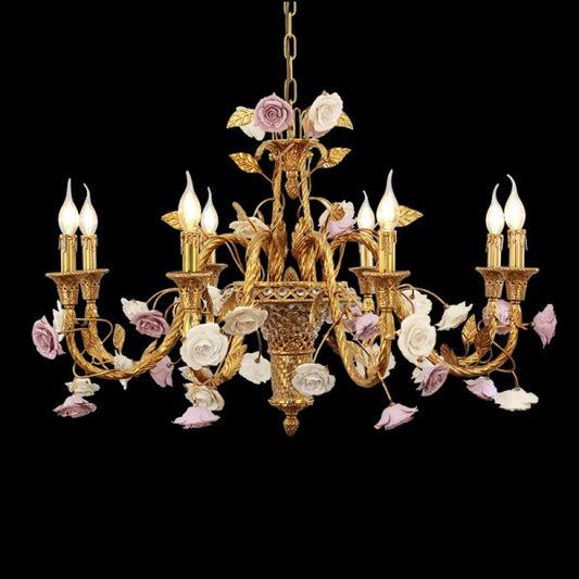 Close-up of vintage brass chandelier with white and lavender ceramic roses, isolated on black.