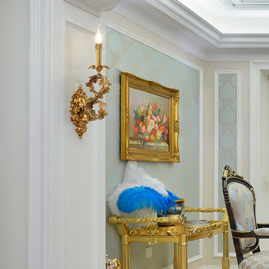 The installed French brass wall lamp on a white wall, paired with a floral oil painting and feather decoration.