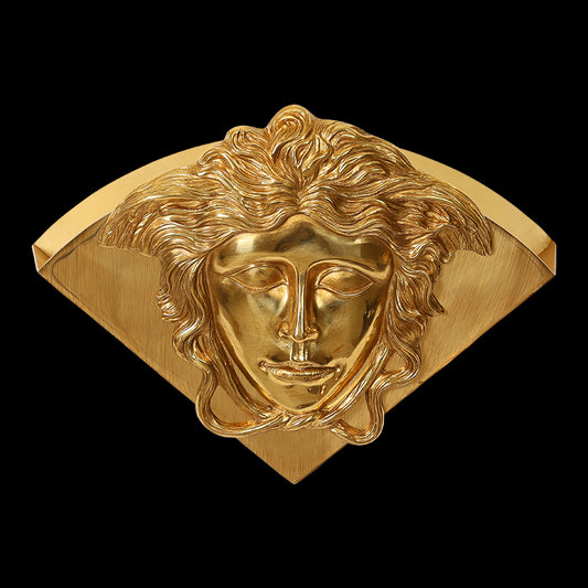 Golden brass wall sconce with a detailed closed-eye human face medallion, brand hallmarks 18K GK visible.