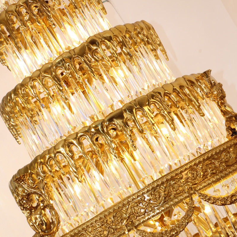 A lit, ornate brass chandelier with crystal cascades against a white wall.