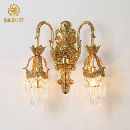 Close-up of the brass sconce’s central engraved medallion and symmetrical crystal cascades.