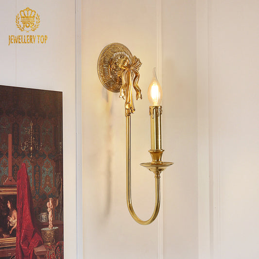 The vintage brass wall lamp installed on a white wall next to a classical painting, emitting a warm glow.