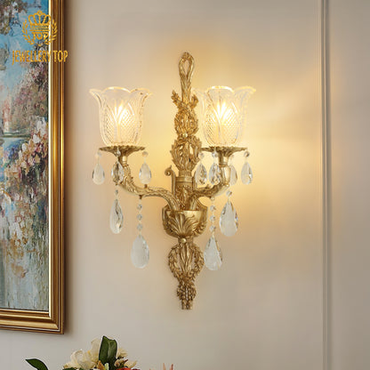 The antique bronze wall lamp installed on a beige wall beside a gold-framed floral painting and decorative vase.