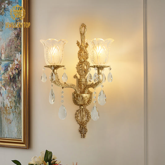 The antique bronze wall lamp installed on a beige wall beside a gold-framed floral painting and decorative vase.