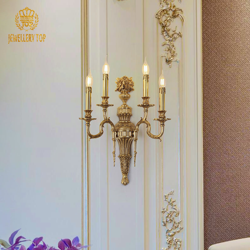 The French decorative brass wall lamp installed on a white paneled wall, brand JEWELLERY TOP visible, emitting warm light.