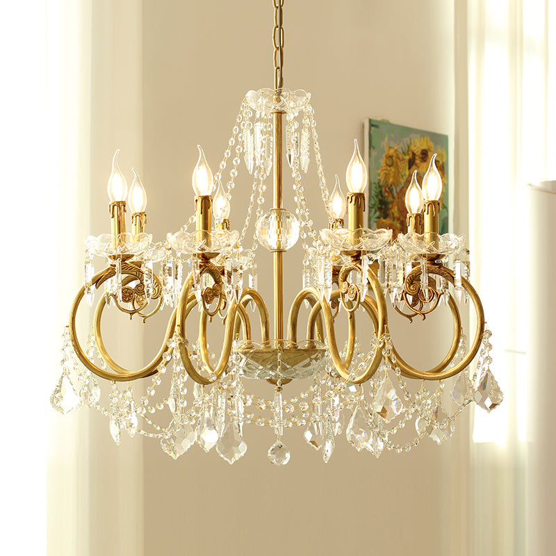A golden french brass chandelier with crystal decorations against a light-colored wall.