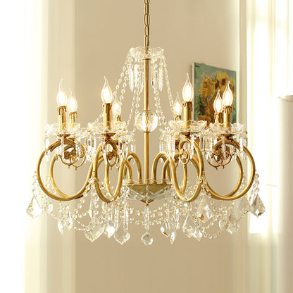 A golden french brass chandelier with crystal decorations against a light-colored wall.