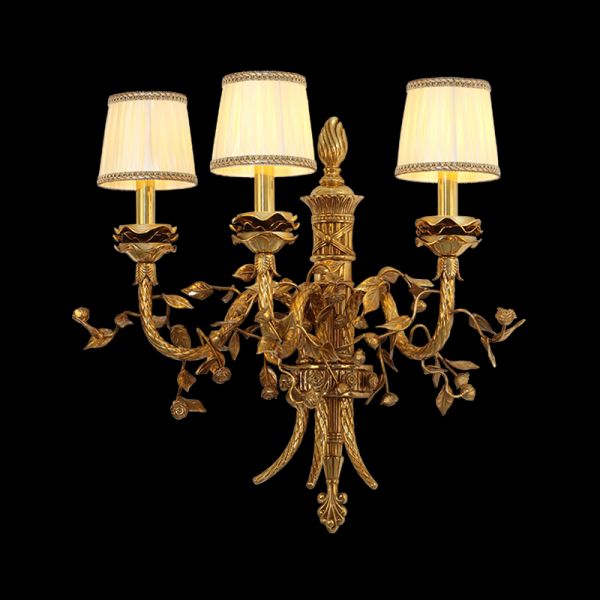 JEWELLERY TOP Renaissance Gourmet brass wall sconce with three fabric shades and grapevine carving, isolated on black.