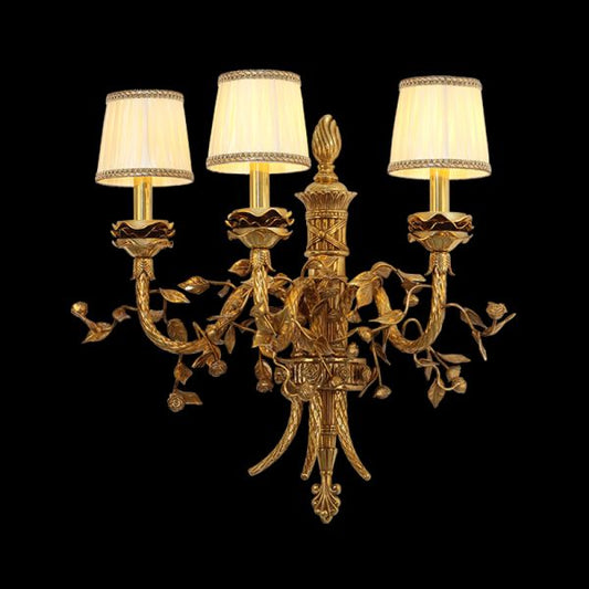 JEWELLERY TOP Renaissance Gourmet brass wall sconce with three fabric shades and grapevine carving, isolated on black.