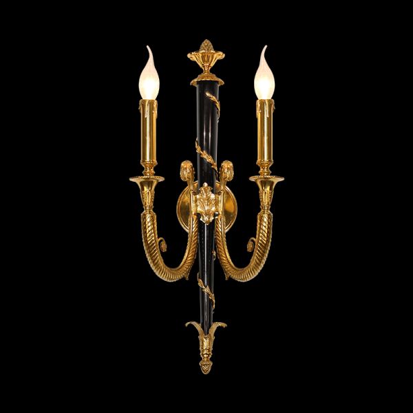 Close-up product shot of the decorative wall sconce showcasing its dual candle arms and ornate brass details on a black background.
