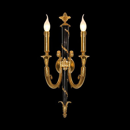 Close-up product shot of the decorative wall sconce showcasing its dual candle arms and ornate brass details on a black background.