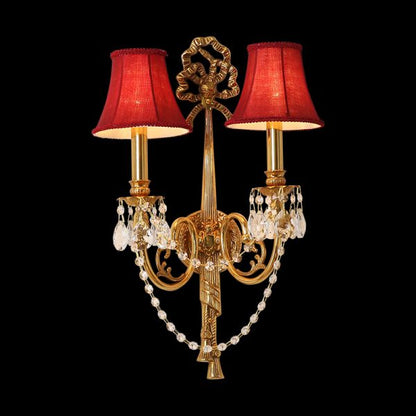 The antique brass wall lamp with red fabric shades and crystal droplets, showcasing its luxurious French design.