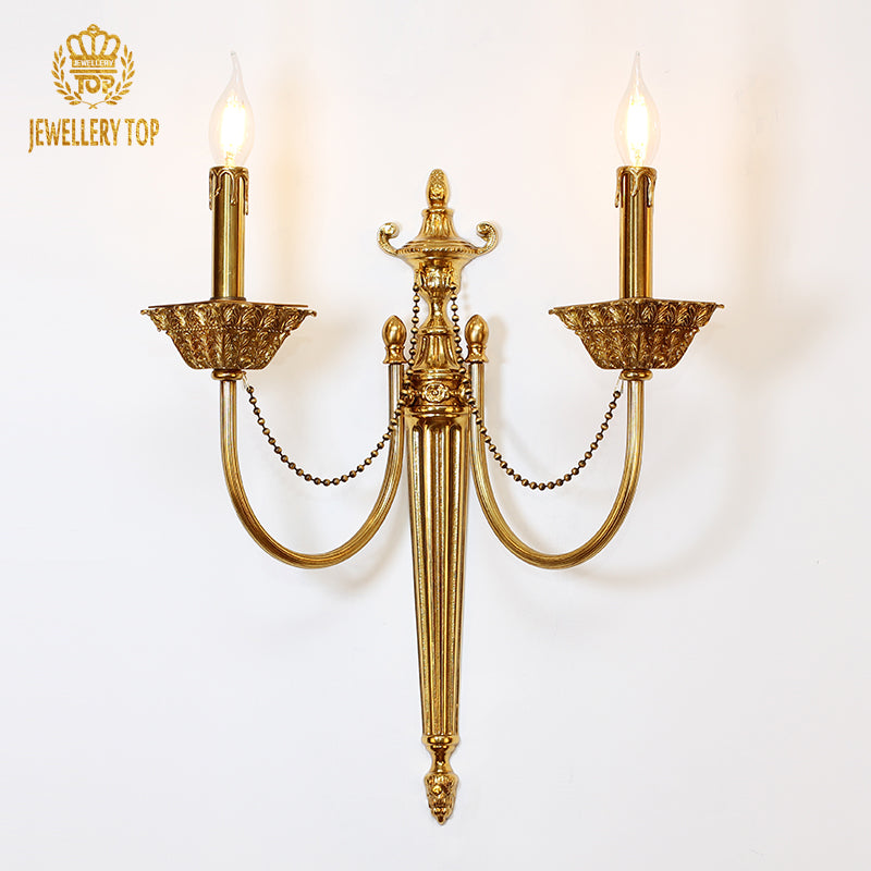 JEWELLERY TOP branded brass wall sconce with ornate central column and lit candles on white background.