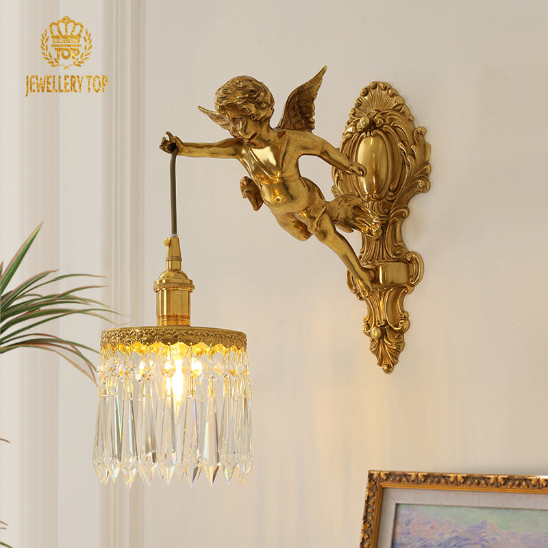 JEWELLERY TOP Golden Cupid Brass Wall Lamp with crystal drops, installed on a light wall beside a green plant and painting.