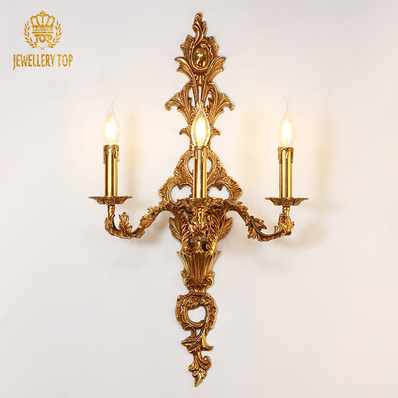 JEWELLERY TOP Triomphe de Versailles three-light brass wall sconce with ornate scrollwork on a white background.