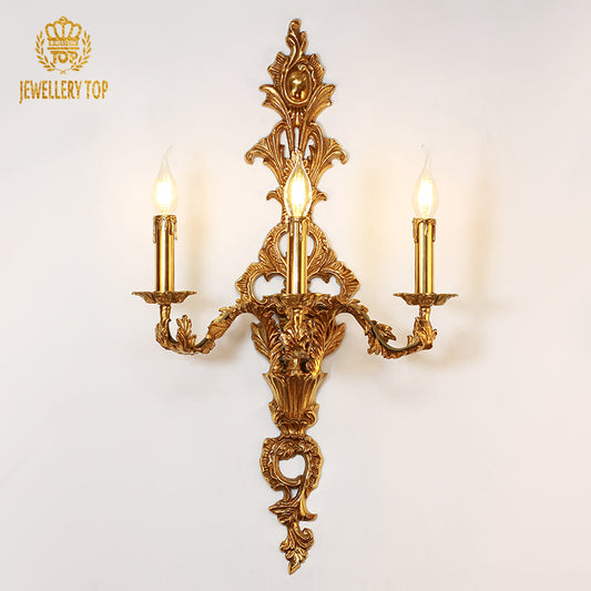 JEWELLERY TOP Triomphe de Versailles three-light brass wall sconce with ornate scrollwork on a white background.
