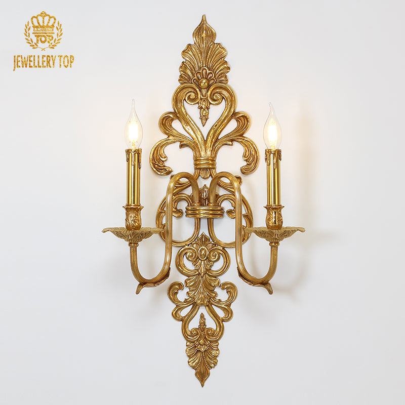 Front view of the golden Symphony No. 2 brass wall sconce with two candle bulbs on a white wall, JEWELLERY TOP branding visible.