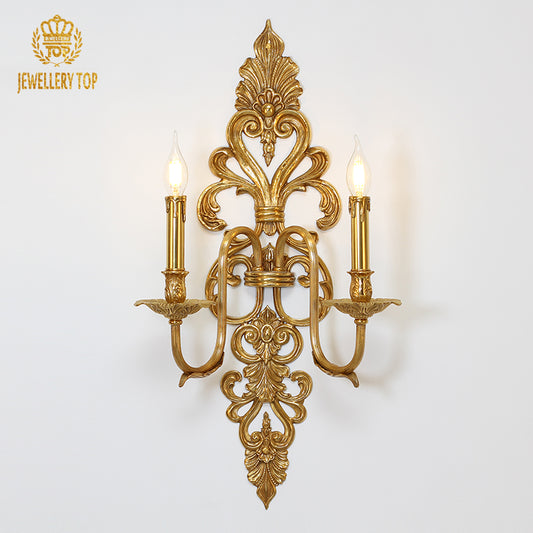 Front view of the golden Symphony No. 2 brass wall sconce with two candle bulbs on a white wall, JEWELLERY TOP branding visible.