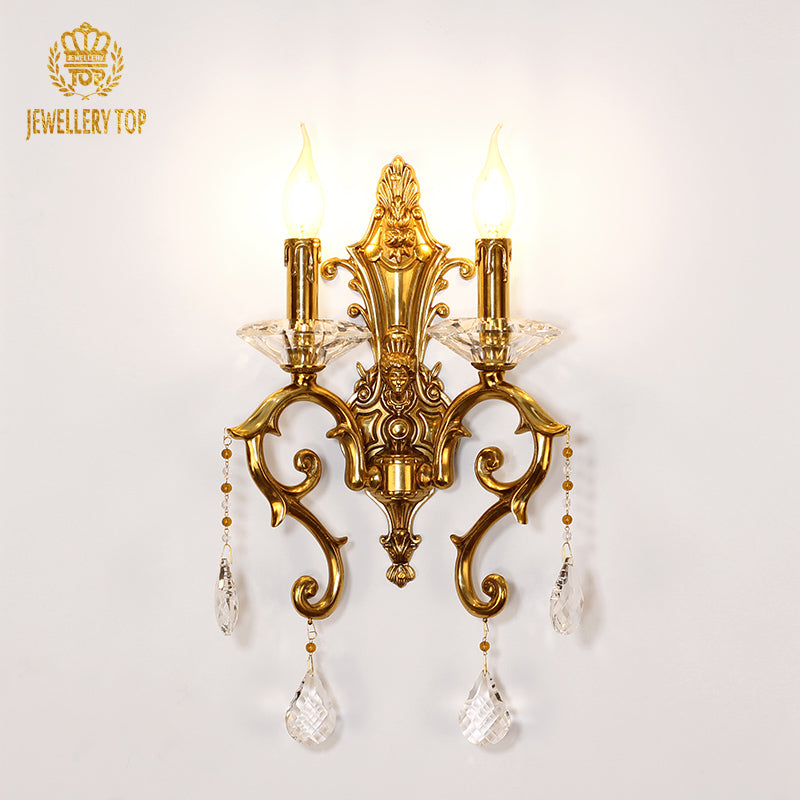 JEWELLERY TOP golden brass wall sconce with two candle bulbs and crystal drops, installed on a white wall.