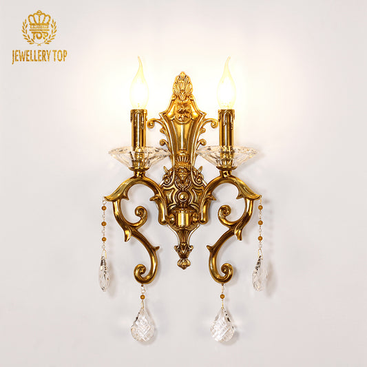 JEWELLERY TOP golden brass wall sconce with two candle bulbs and crystal drops, installed on a white wall.