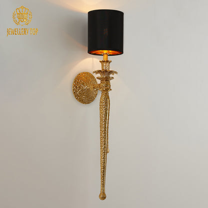 JEWELLERY TOP Noir Cylindre brass wall lamp with black cylindrical shade on a light wall, showcasing brand logo.