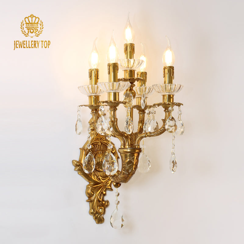 JEWELLERY TOP branded five-arm golden brass wall sconce with crystal drops, installed on a white wall.