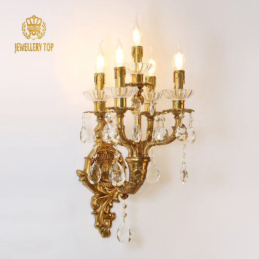 JEWELLERY TOP branded five-arm golden brass wall sconce with crystal drops, installed on a white wall.