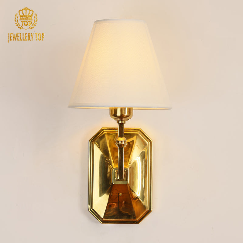 The golden home wall lamp with a white shade, highlighting its elegant profile and soft glow in a cozy interior setting.