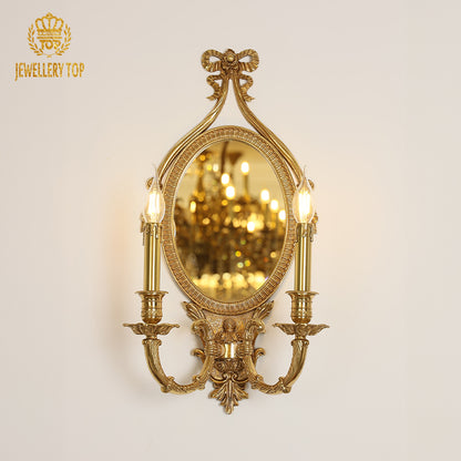 Branded golden French wall lamp installed on a light wall, showcasing its ornate bow, mirror, and twin candle bulbs.