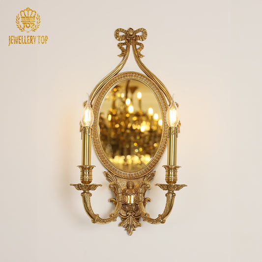 Branded golden French wall lamp installed on a light wall, showcasing its ornate bow, mirror, and twin candle bulbs.