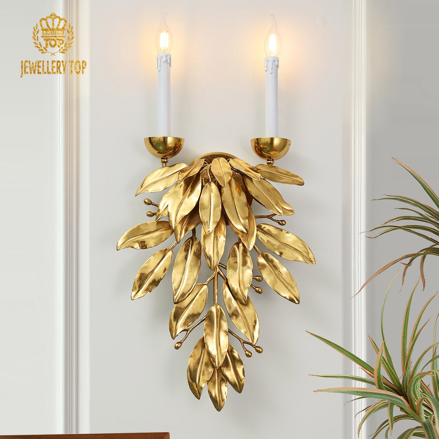 JEWELLERY TOP Forêt Dorée brass wall sconce with cascading golden leaves and two lit candle bulbs on a light wall.
