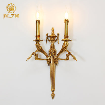 JEWELLERY TOP Eclat Double Arm brass wall sconce installed on a white wall, emitting warm light from two bulbs.