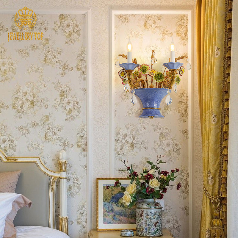 The luxury decorative wall light installed in a bedroom, glowing beside a gold-trimmed headboard and floral wallpaper.
