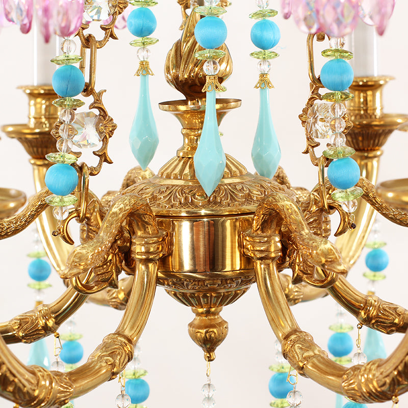 Macro close-up of ornate brass scrollwork, candle bulbs, and hanging blue and pink crystal strands.