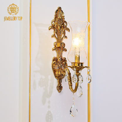 Extreme close-up of the ornate brass scrollwork and the brand’s crown logo on the sconce.