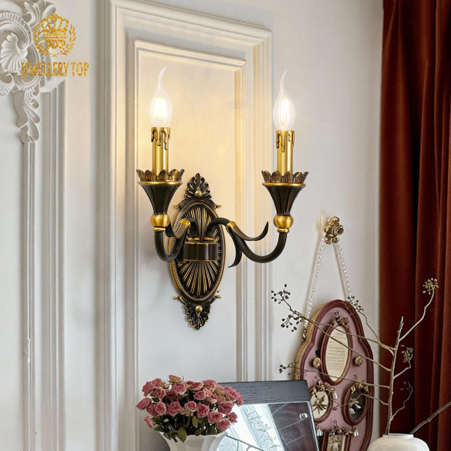 The ornate hotel wall light installed on a white wall with a decorative mirror and pink peonies nearby.