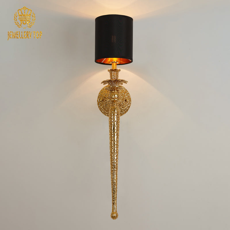 Product close-up of the golden brass wall lamp with intricate textured base and a black fabric lampshade.