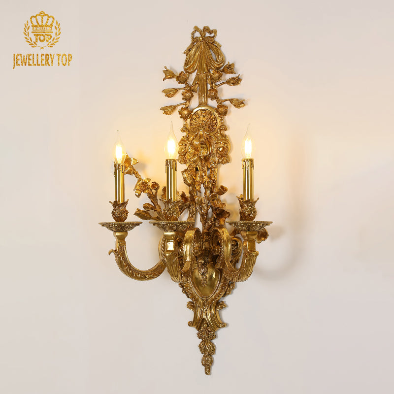 Detailed product shot of the golden luxury bronze wall light with four candle bulbs and intricate floral carvings.