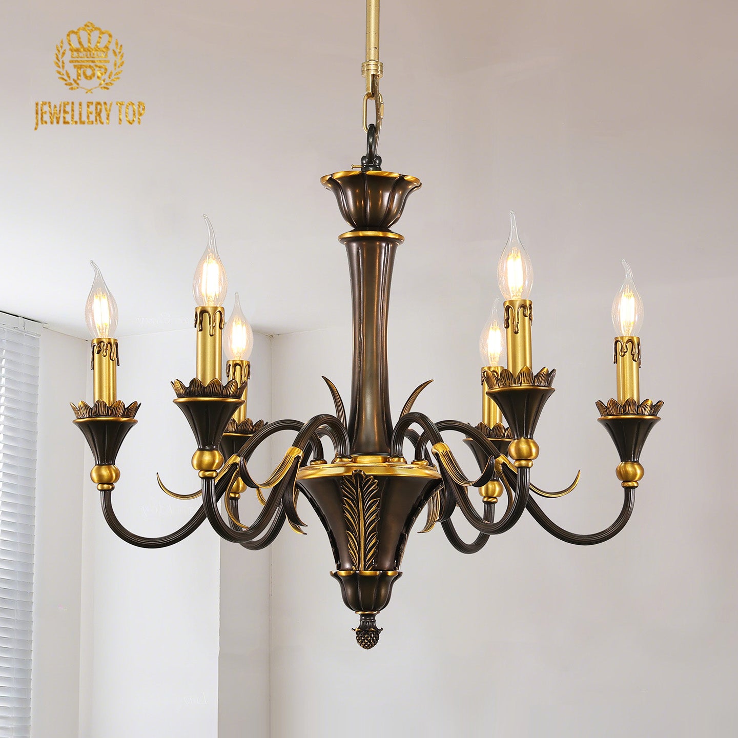 JEWELLERY TOP's golden brass chandelier with candle bulbs against a white wall and shutters.