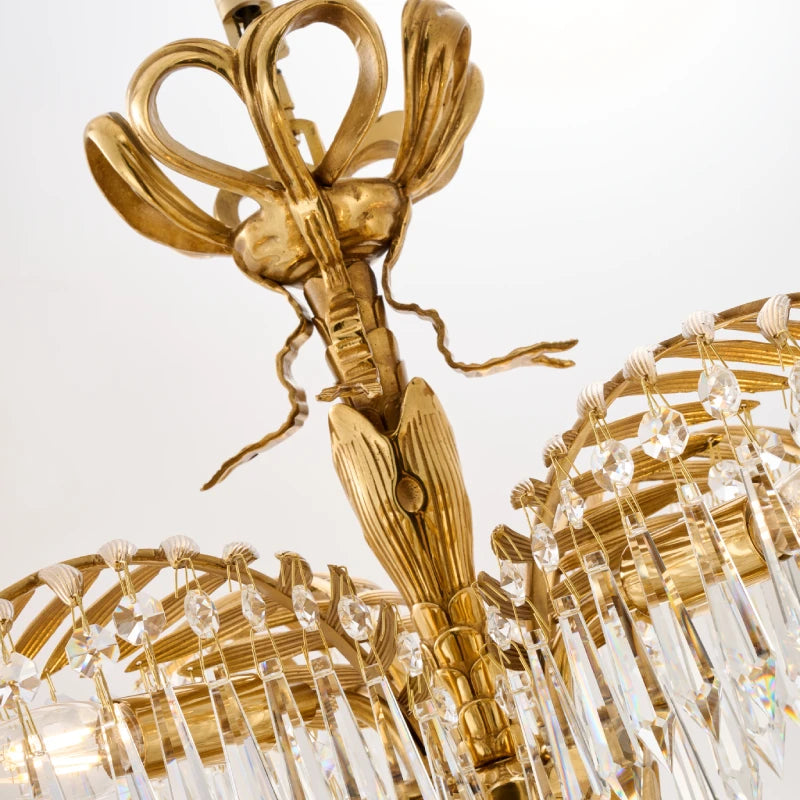Close-up detail of brass palm frond arm and hanging crystal droplets on a luxury chandelier.