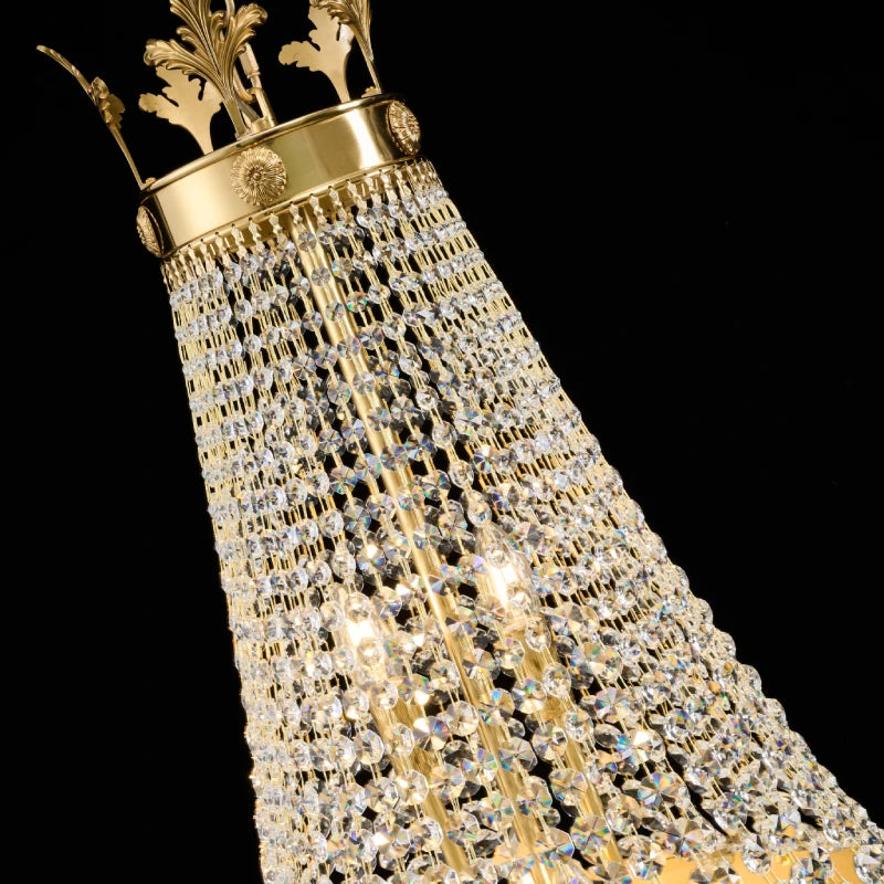 Extreme close-up of the ornate crown-shaped brass top with sunburst emblems on a crystal chandelier.