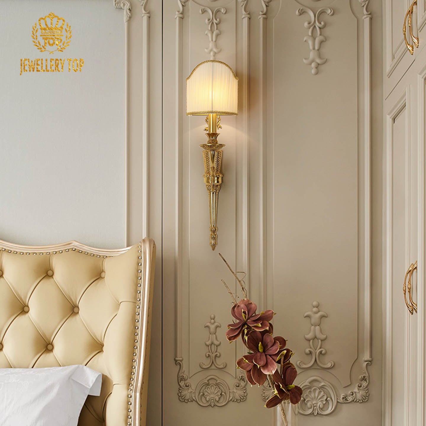 The French classical brass wall lamp installed in an elegant bedroom beside a tufted headboard and floral decor.
