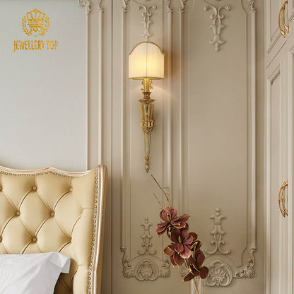 The French classical brass wall lamp installed in an elegant bedroom beside a tufted headboard and floral decor.