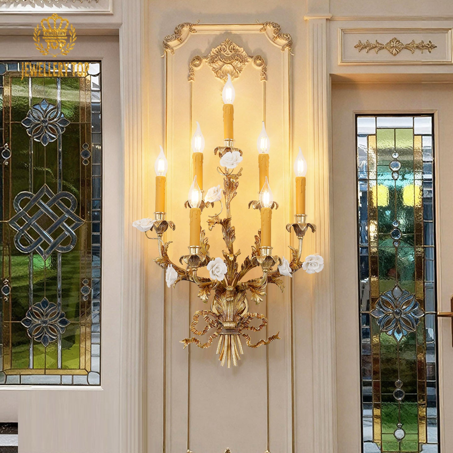 Lifestyle interior shot of the ornate 7-light sconce in a luxurious room with a crystal chandelier visible through a doorway.