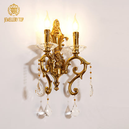 Close-up branded product shot (JEWELLERY TOP) of the ornate brass sconce with lit candle-style bulbs.