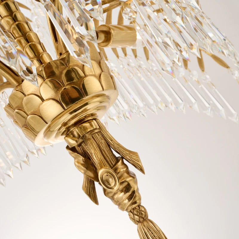Macro shot of intricate scaled brass texture and crystal tassel on a palm leaf chandelier.
