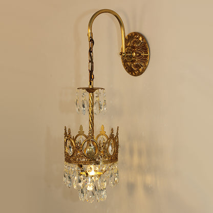 Close-up detail of the ornate brass scrollwork and faceted crystal strands on the luxury bedside wall lamp.
