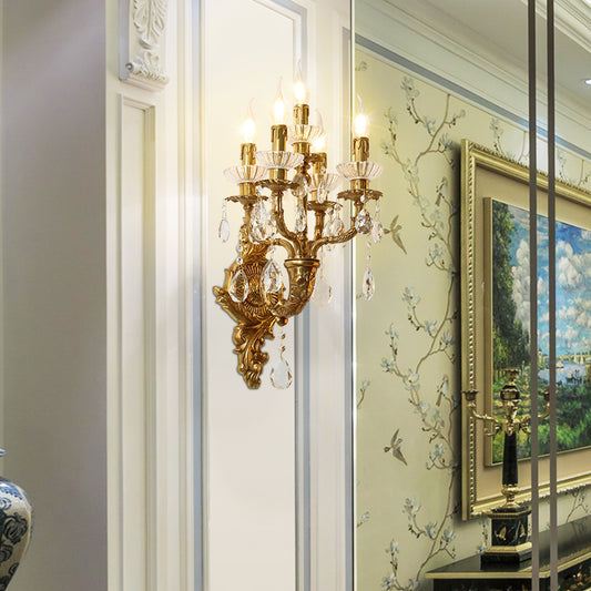 Front view of the ornate French luxury brass candelabra sconce with lit bulbs, beside a gilded framed painting.